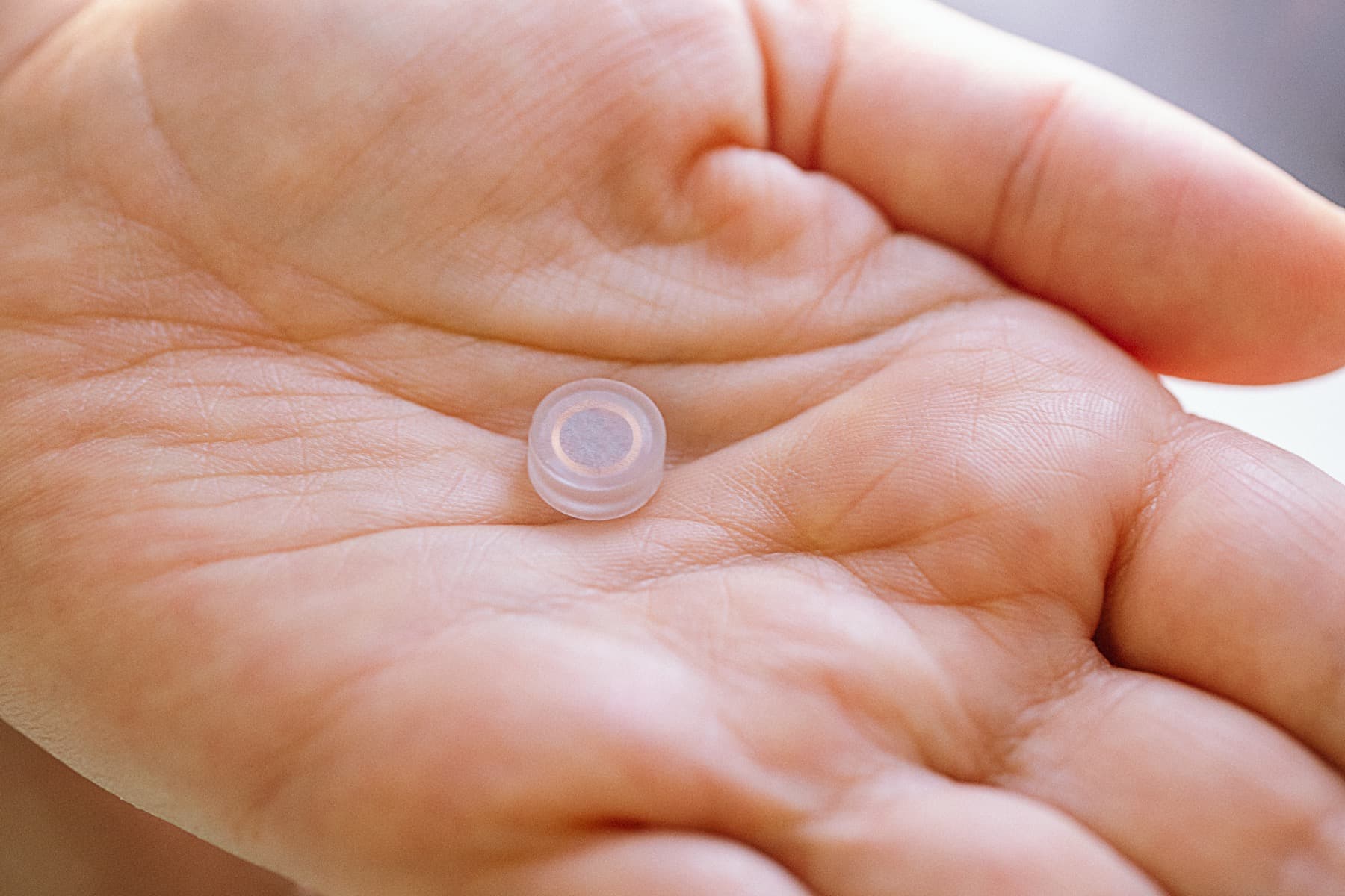 A tiny hermetic glass implant resting in the palm of a hand